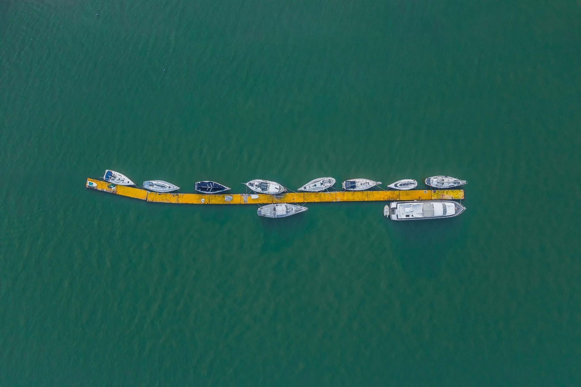 Aerial view of boats docked along a curvy yellow floating pier on sea near Sunway Hotel Big Box
